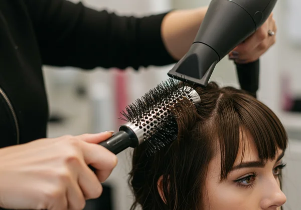 Person styling bangs with a blow dryer and small round brush